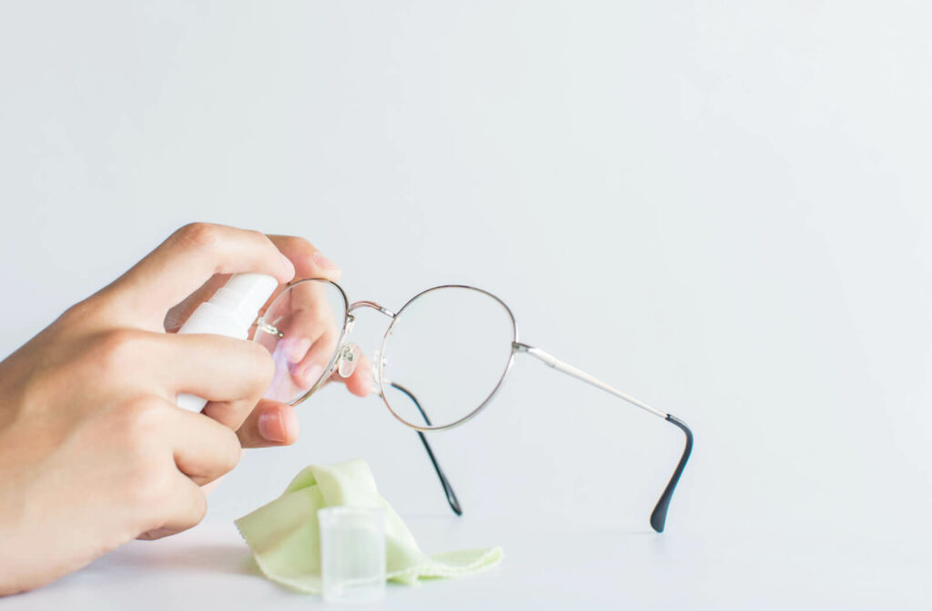 A girl hands cleaning eyeglasses with cleaning spray and a microfibre cloth.