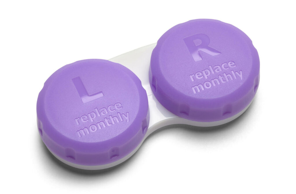 A pair of contact lenses in a purple container with reminder notes to replace monthly.