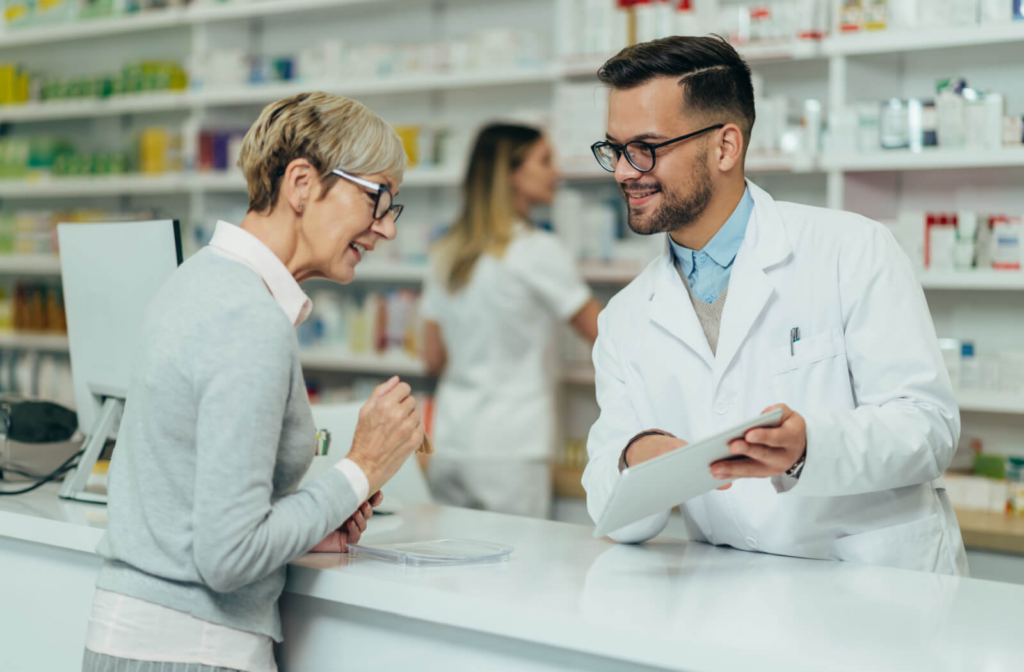 A young pharmacist showing the contents of his digital tablet to a middle-aged woman.