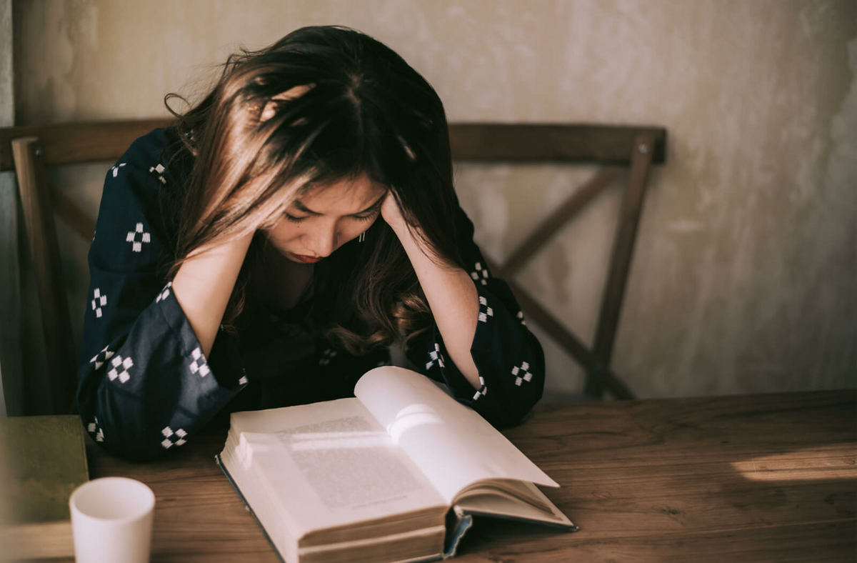 A young woman suffering from a headache while reading a book.