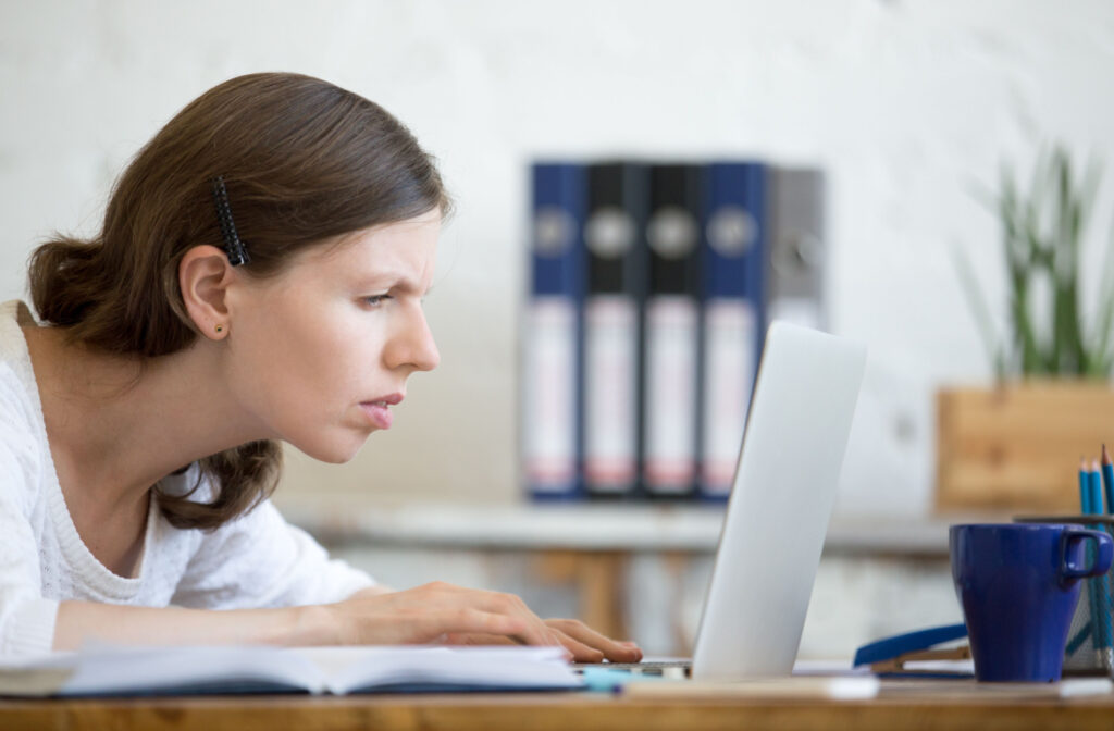 A woman leaning closer to her laptop screen to see its contents better.