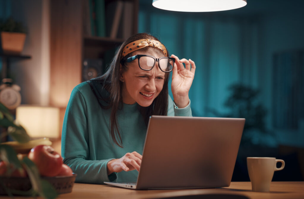 A woman adjusting her eyeglasses upwards and squinting towards her laptop.