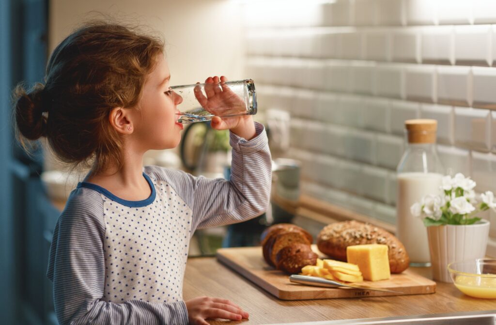 A girl in her pyjamas drinking water from a glass.