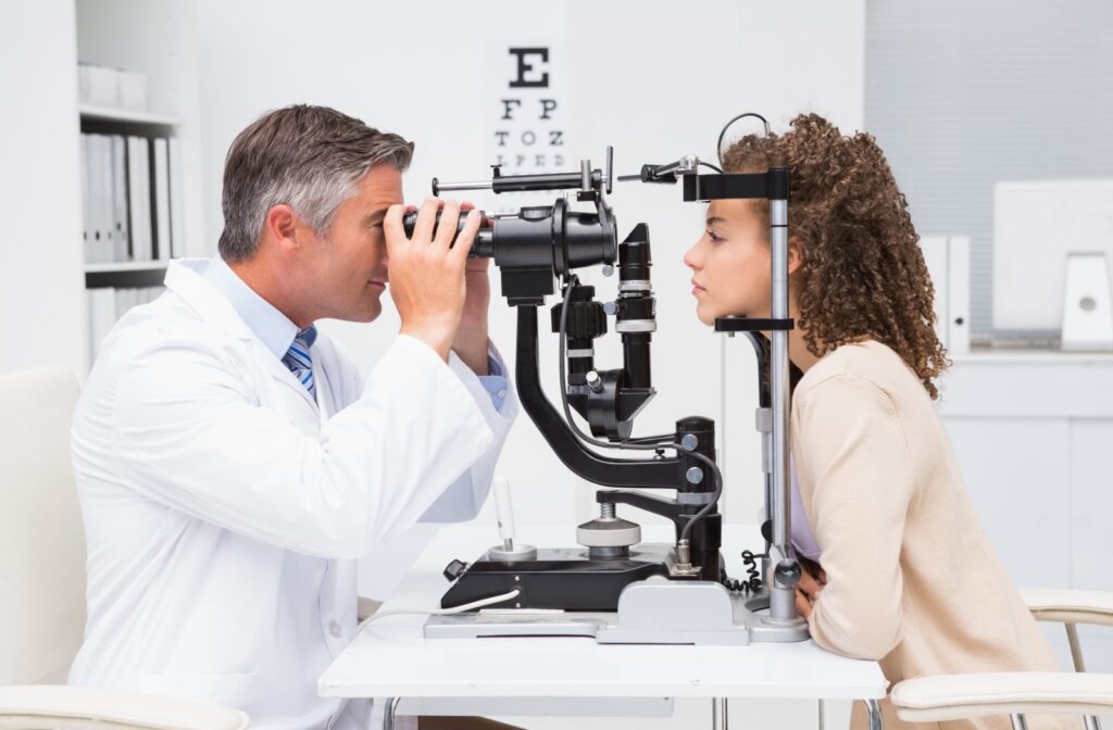 A smiling male optometrist carefully examines a female patient's eyes.