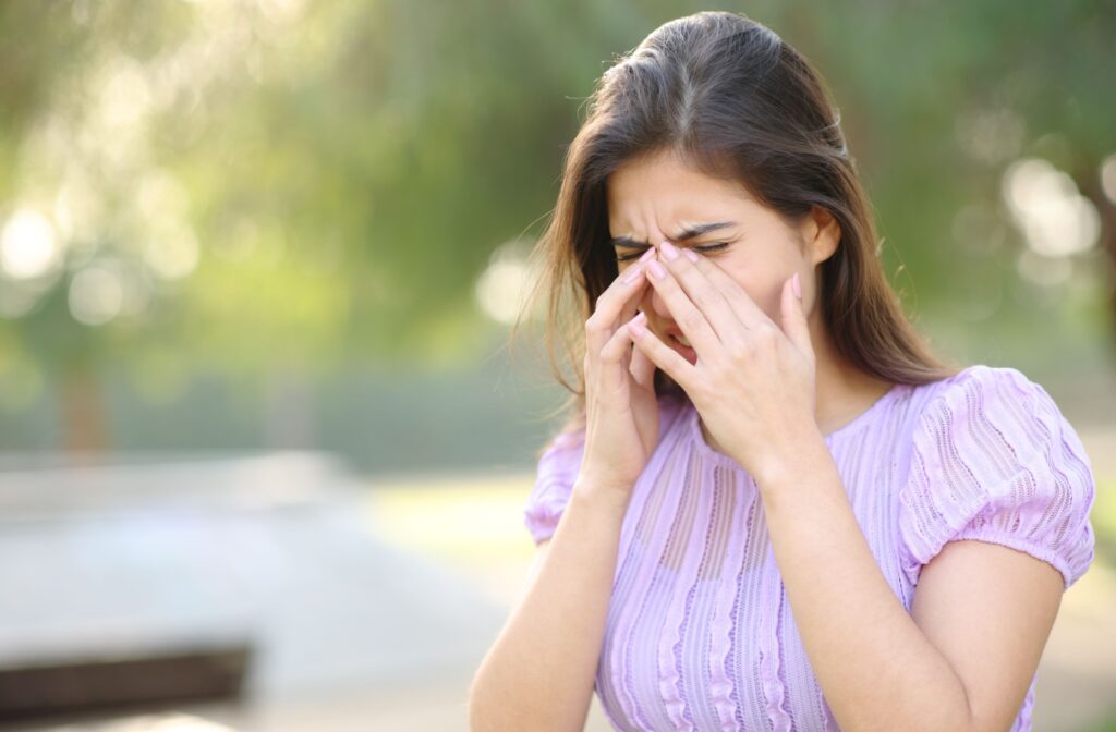 A woman with allergies rubbing her eyes in a park.