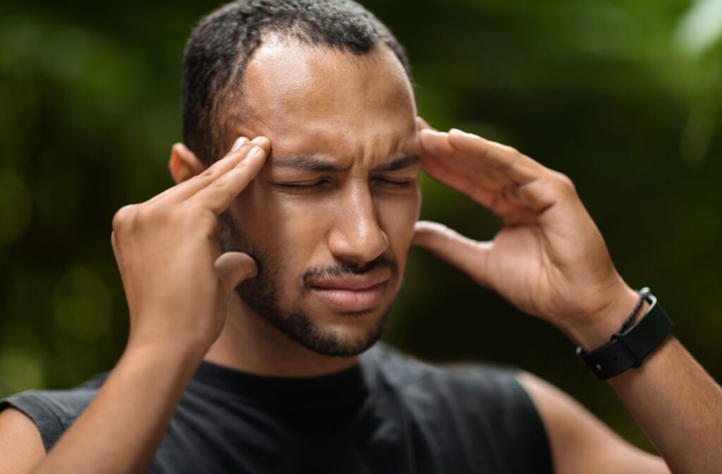 A man with eyes tightly closed touching their temples with both hands from a headache.