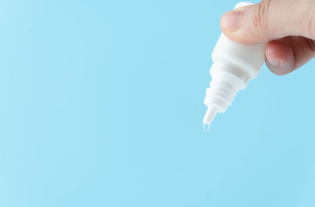 A bottle of eye drops with a drop coming out from the end